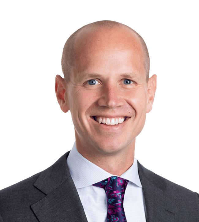 Head-and-shoulders portrait of a smiling man in a dark suit and purple tie.